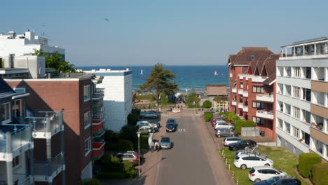 Aerial-view-flying-between-building-street-facing-Baltic-clear-blue-sea-water-in-Scharbeutz,-Germany,-dolly-in,-day